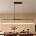 Minimalist black linear LED pendant light glowing warmly in a kitchen with warm beige cabinets, a walnut table and chocolate brown leather chairs