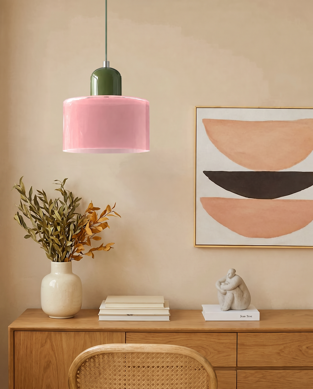 Blush pink glass drum pendant light with olive top above an oak sideboard against a warm beige wall