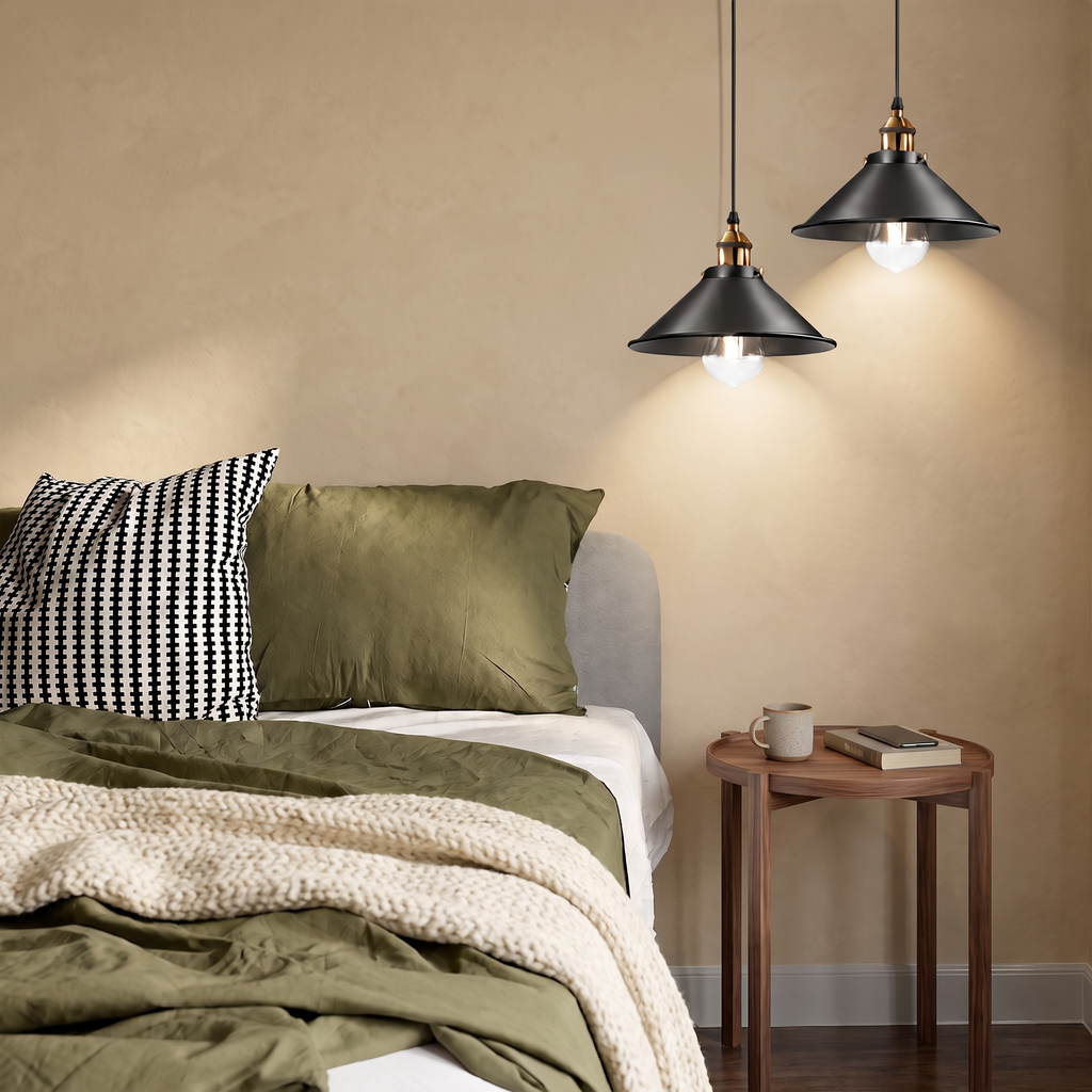 Two black and brass industrial cone pendant lights beside a bed with olive green linen against a warm beige wall