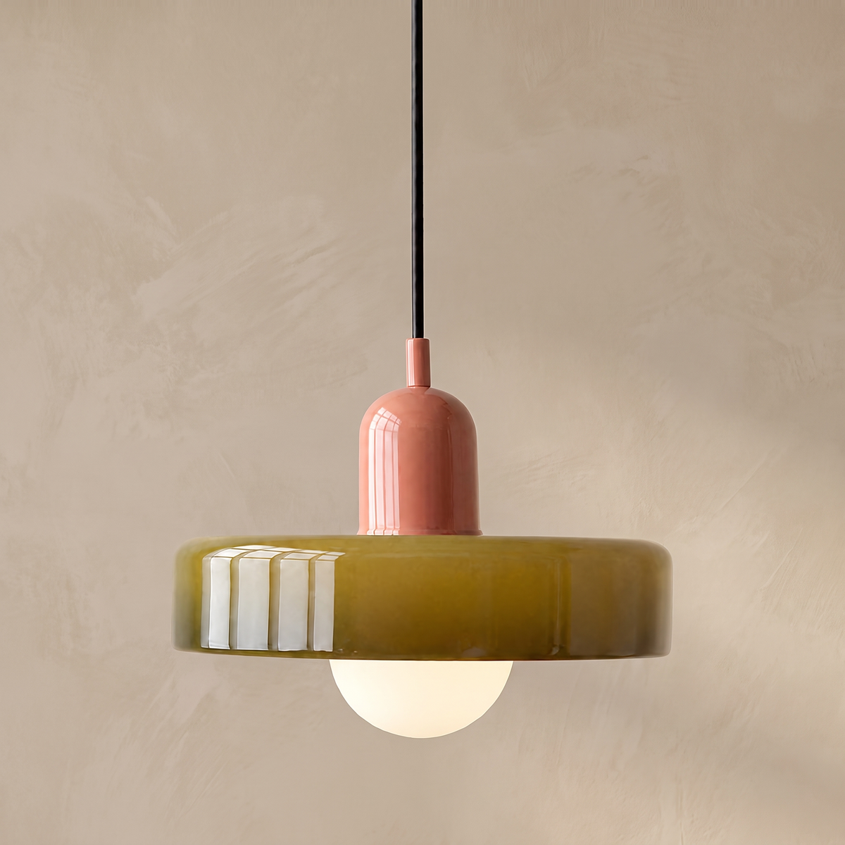 Olive glass disc pendant light with pink top against a warm beige limewash wall