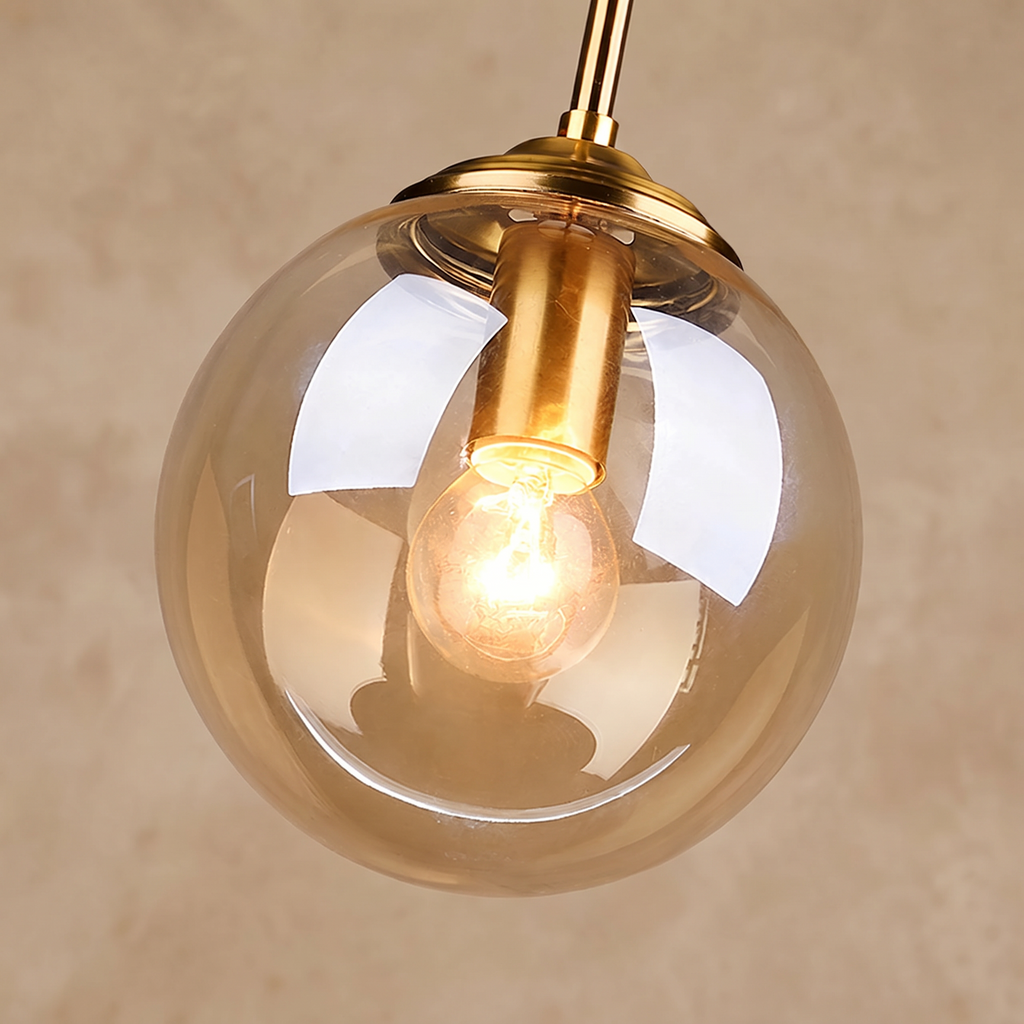 Close-up of the amber glass globe and brass holder against a warm beige wall