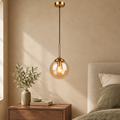 Single amber glass globe pendant with brass stem beside a walnut bedside table in a warm beige bedroom