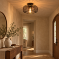 Black wire cage ceiling light glowing in a warm beige hallway with walnut console